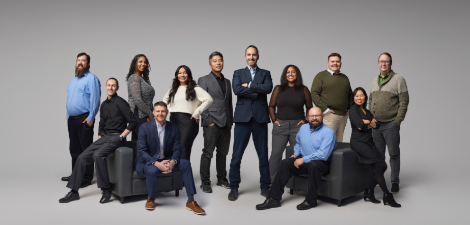 Group of diverse professionals, posing in business attire against a gray backdrop.