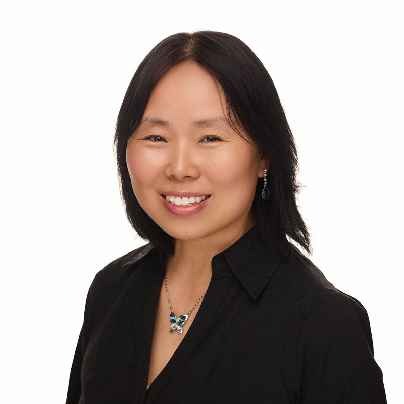 Woman with black hair smiling, wearing a black shirt and necklace, white background.