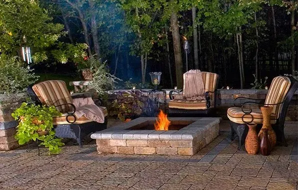 Outdoor seating area with a lit fire pit and wicker chairs at dusk.