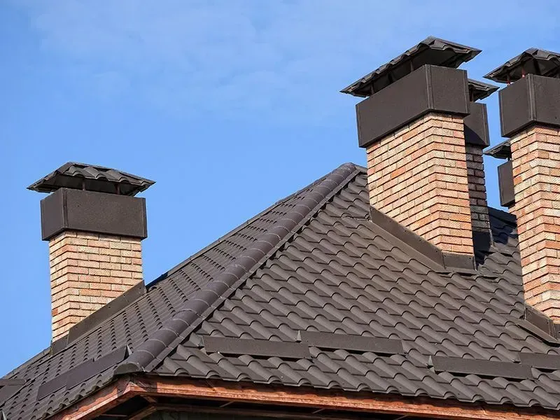 Brown tile roof with brick chimneys against a blue sky.