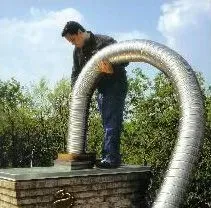 Man on a roof installing a large, flexible silver duct onto a brick structure outdoors.