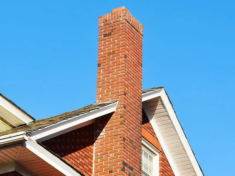 Brick chimney on a residential house against a clear blue sky.
