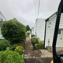 A path under construction next to a house with a large bush and a work vehicle.