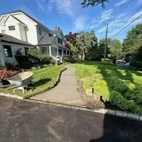 A large white house with a landscaped yard and a concrete path. A wheelbarrow sits on the grass.