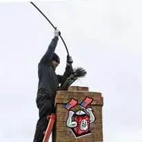 Chimney sweep cleaning a chimney, holding a brush, with a patriotic logo on the chimney.