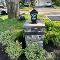 Stone lamp post with a black lamp, surrounded by bushes and grass.