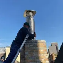 Man installing a chimney cap on a brick chimney against a blue sky.