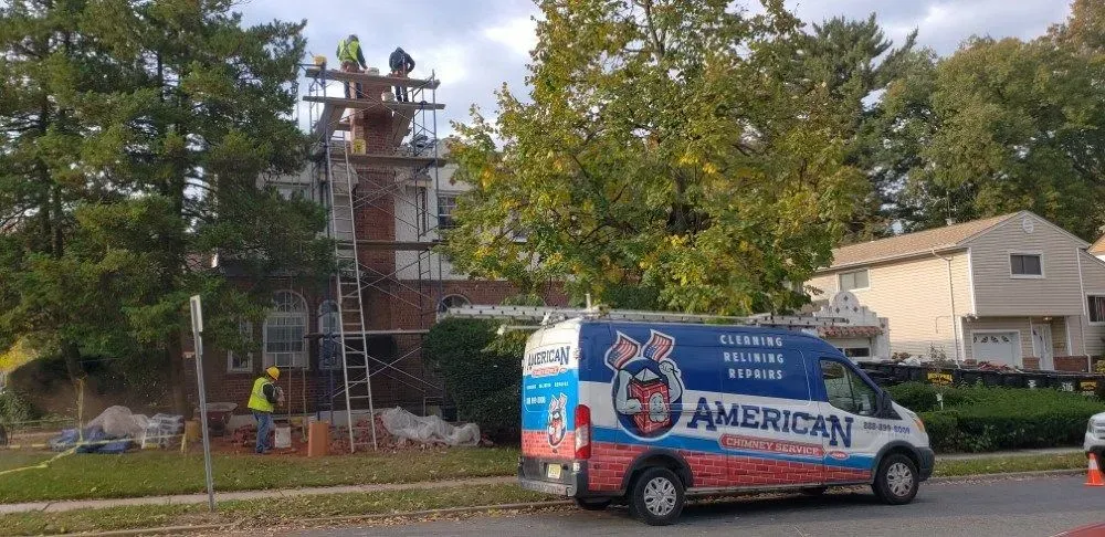 Workers on a roof, chimney repair. American service van parked on the street.