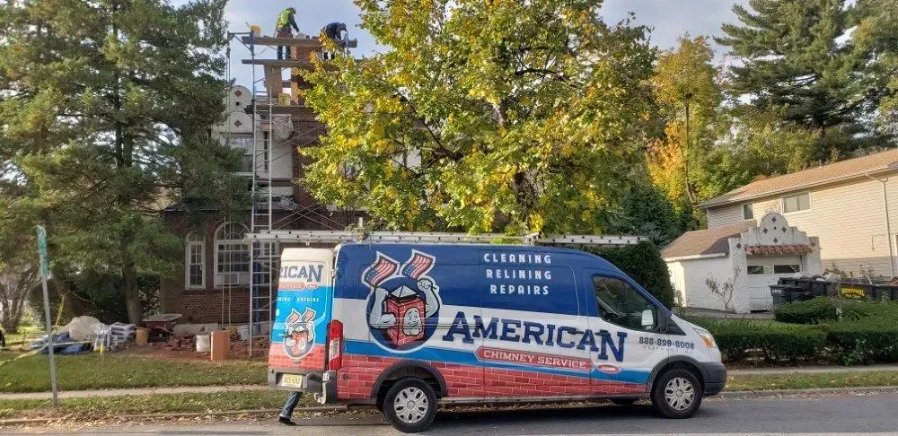 A repair van in front of a house, and workers on the roof fixing the chimney.