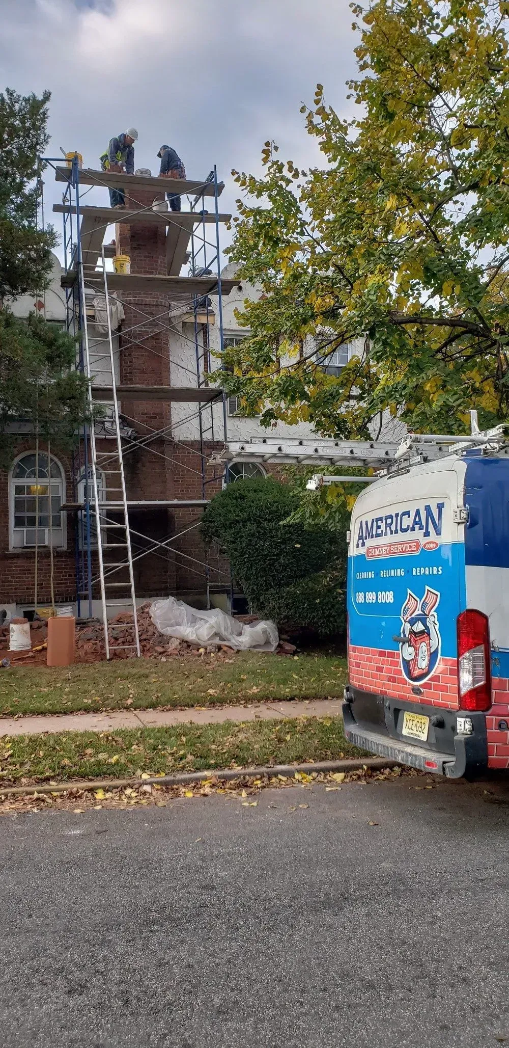 Building under construction with scaffolding, workers on the roof, van in front with American Service logo.