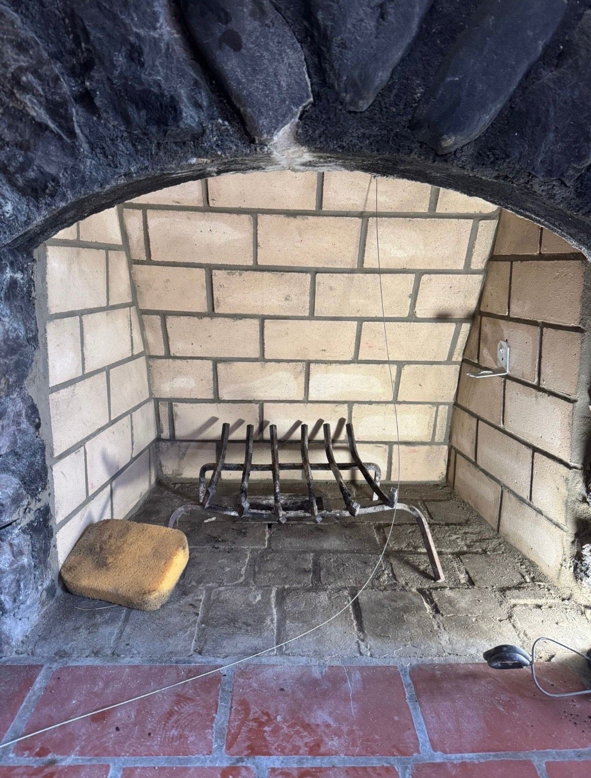 Fireplace with brick interior, metal grate, and arched stone surround. A sponge sits inside.