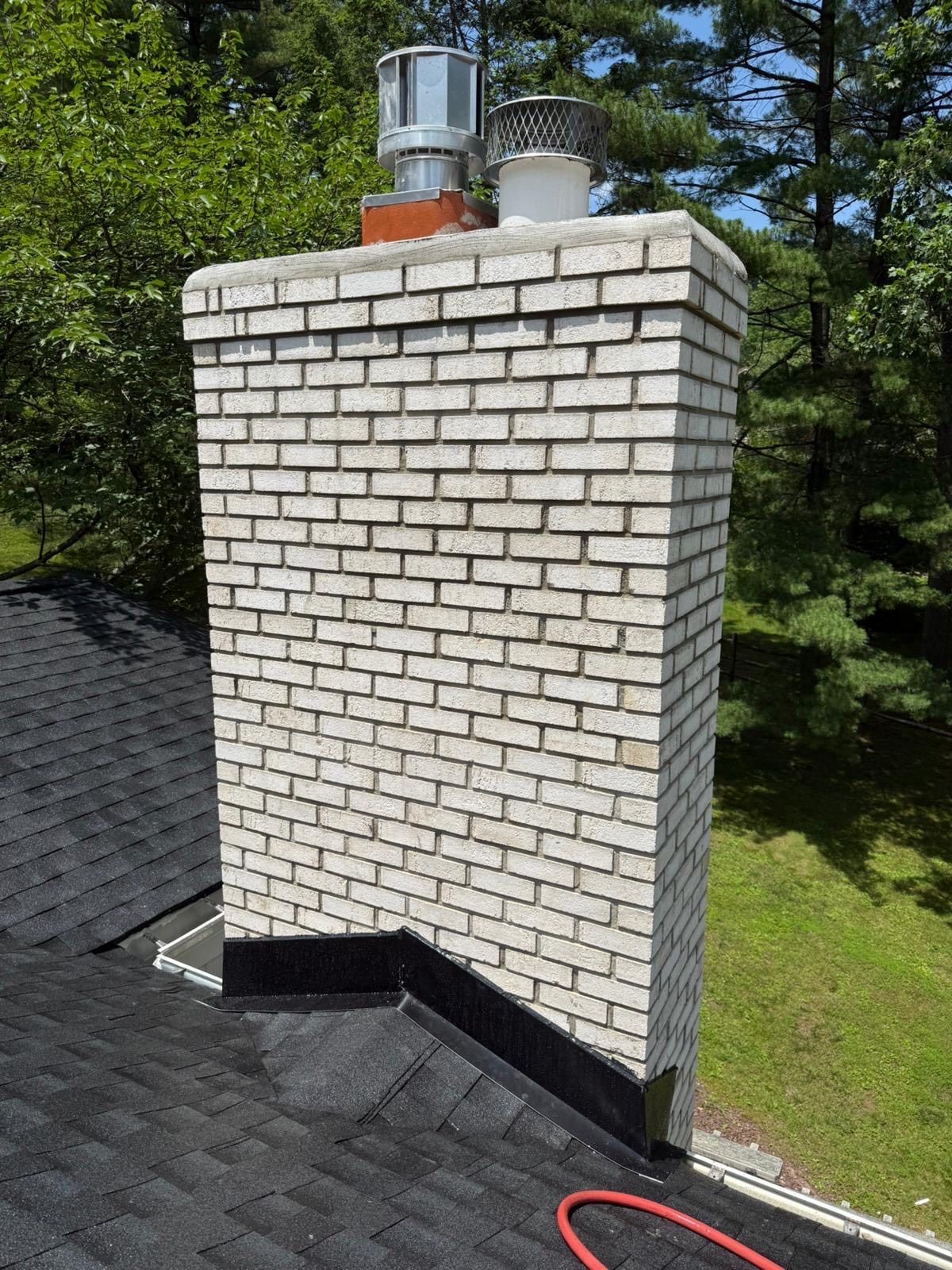 Brick chimney on a black shingled roof, with two metal chimney caps.