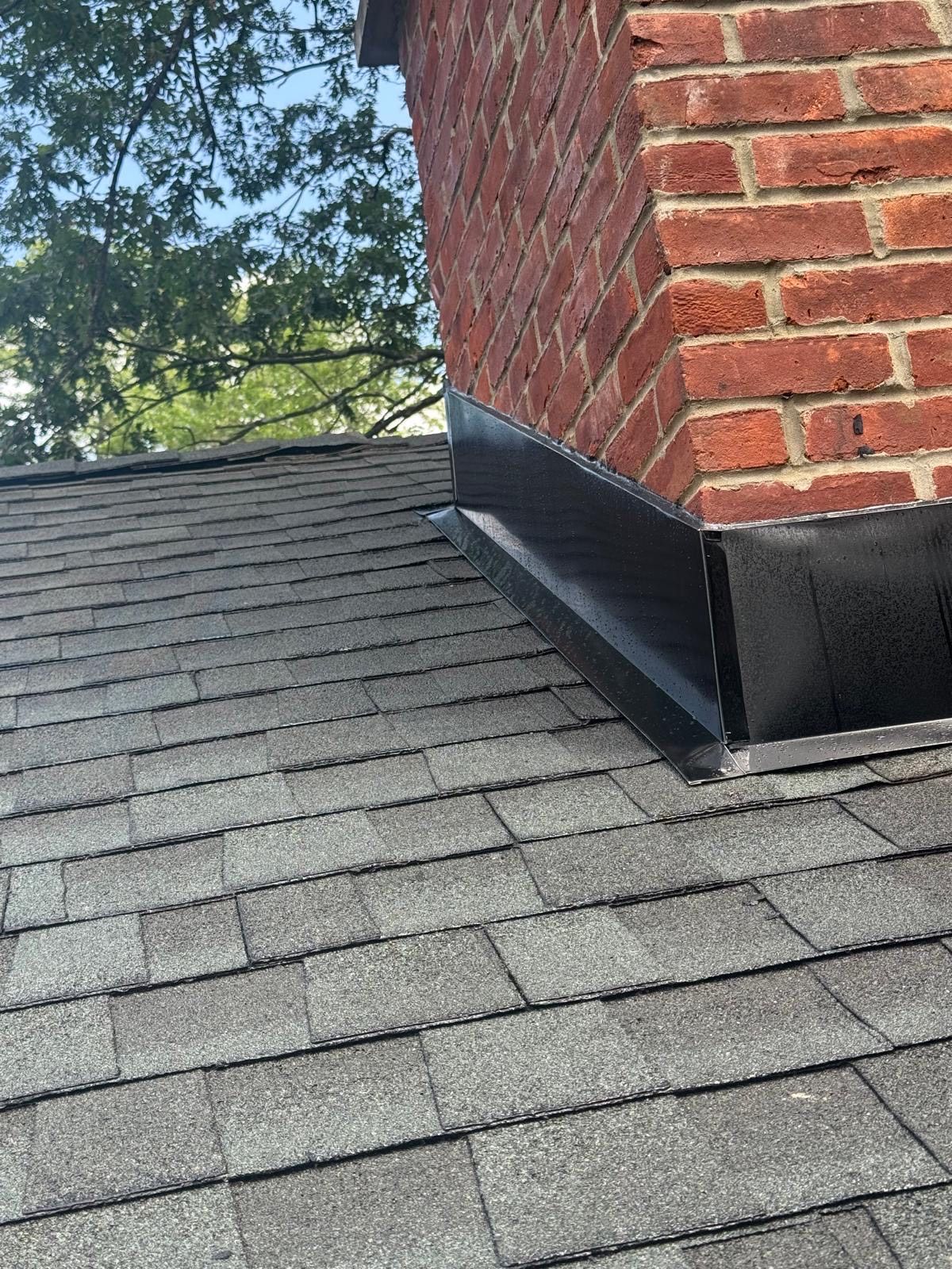 Brick chimney on a gray shingle roof, with black flashing.