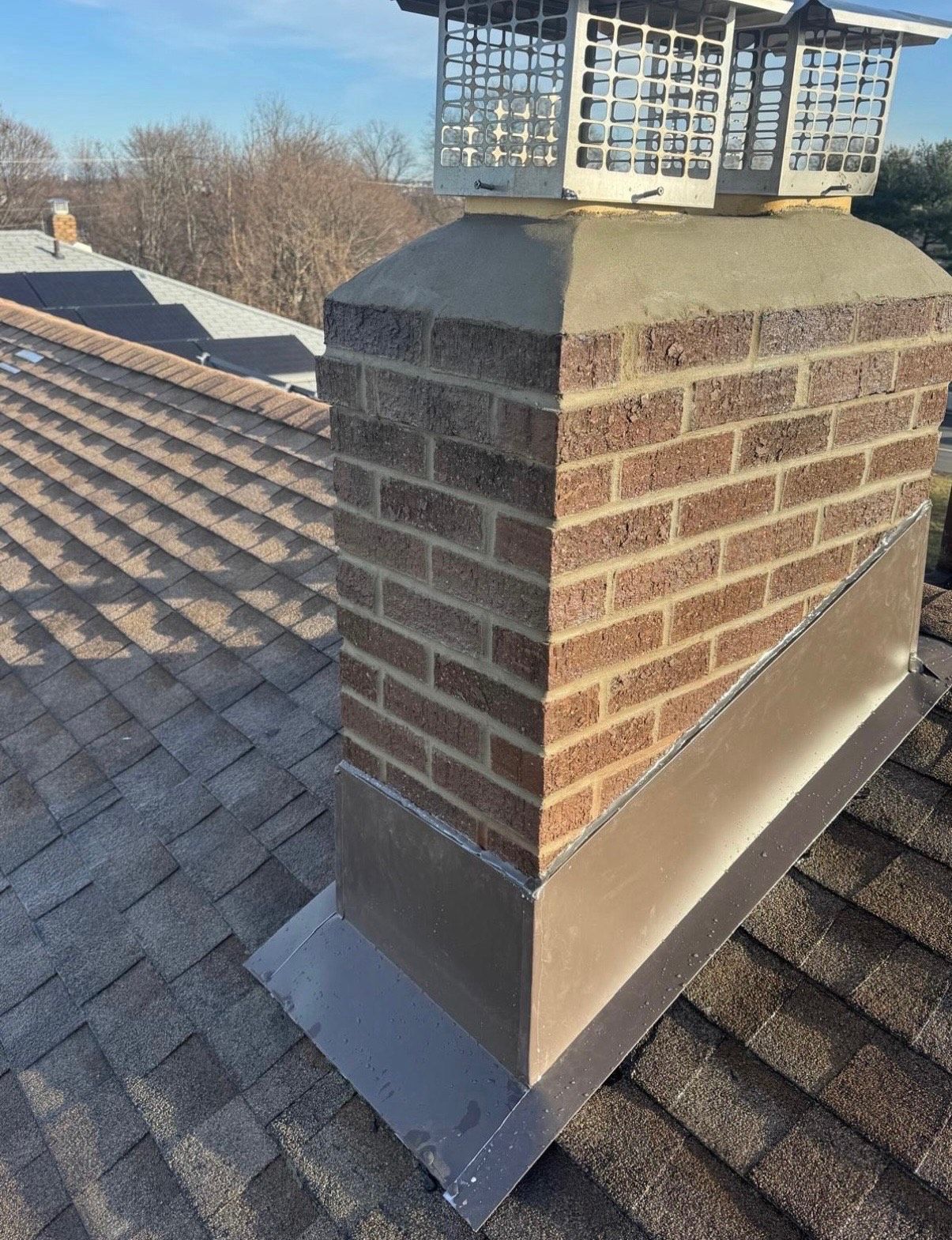 Brick chimney on a shingled roof with metal flashing and a metal chimney cap.