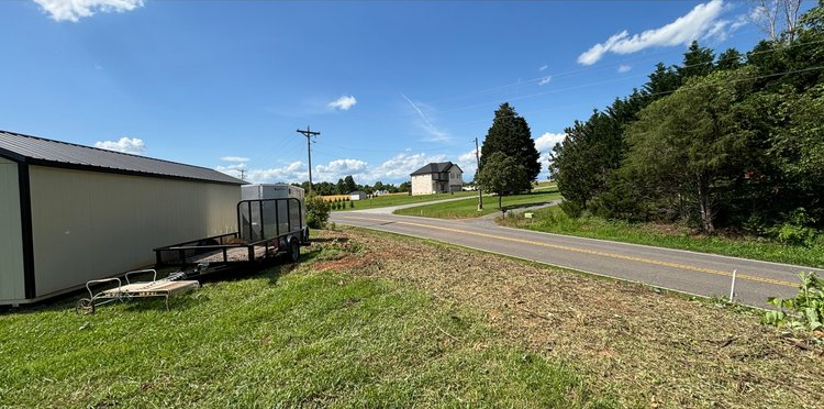 A trailer is parked in the grass next to a road.