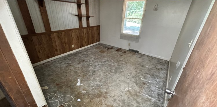 An empty room with a carpeted floor and a window.