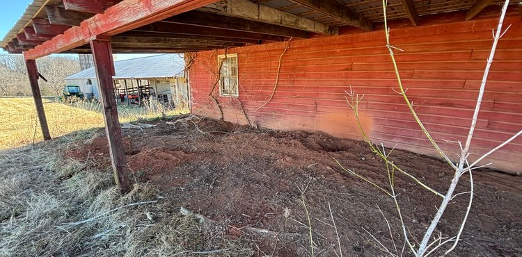 A red barn with a lot of dirt underneath it.