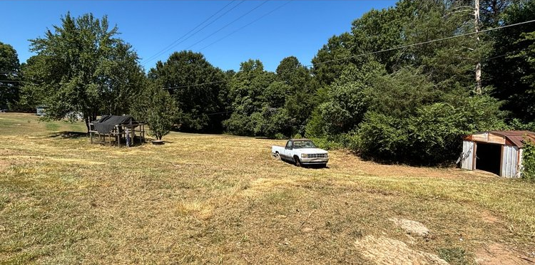 A white truck is parked in a field with trees in the background.