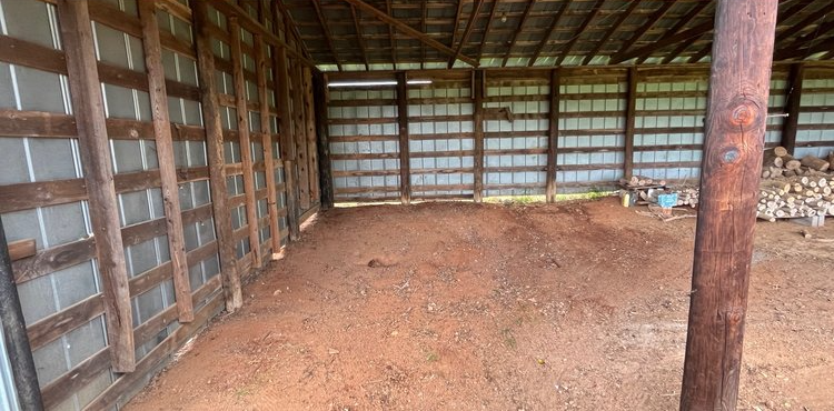 An empty barn with a lot of dirt in it.
