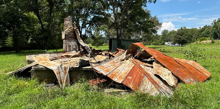 A rusty metal roof is sitting in the middle of a grassy field.