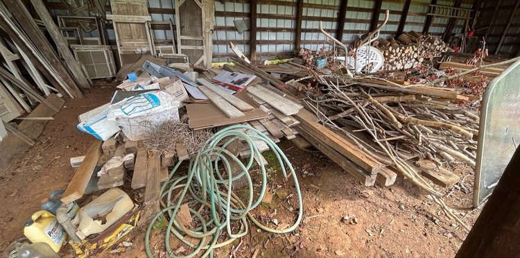 A pile of wood and a hose in a barn.