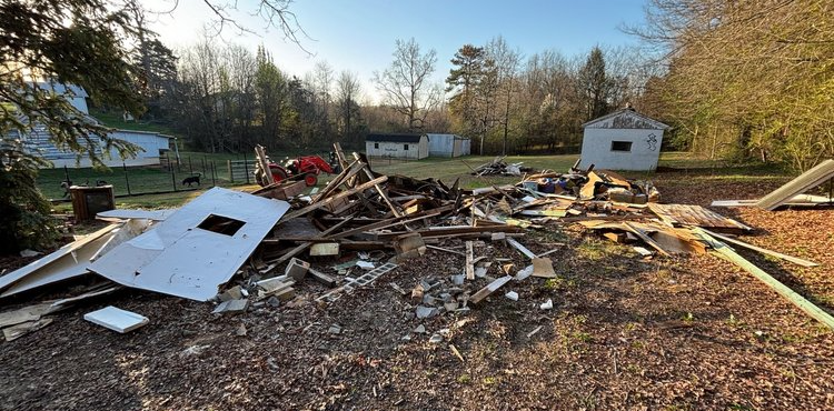 A pile of rubble in a yard with a shed in the background.