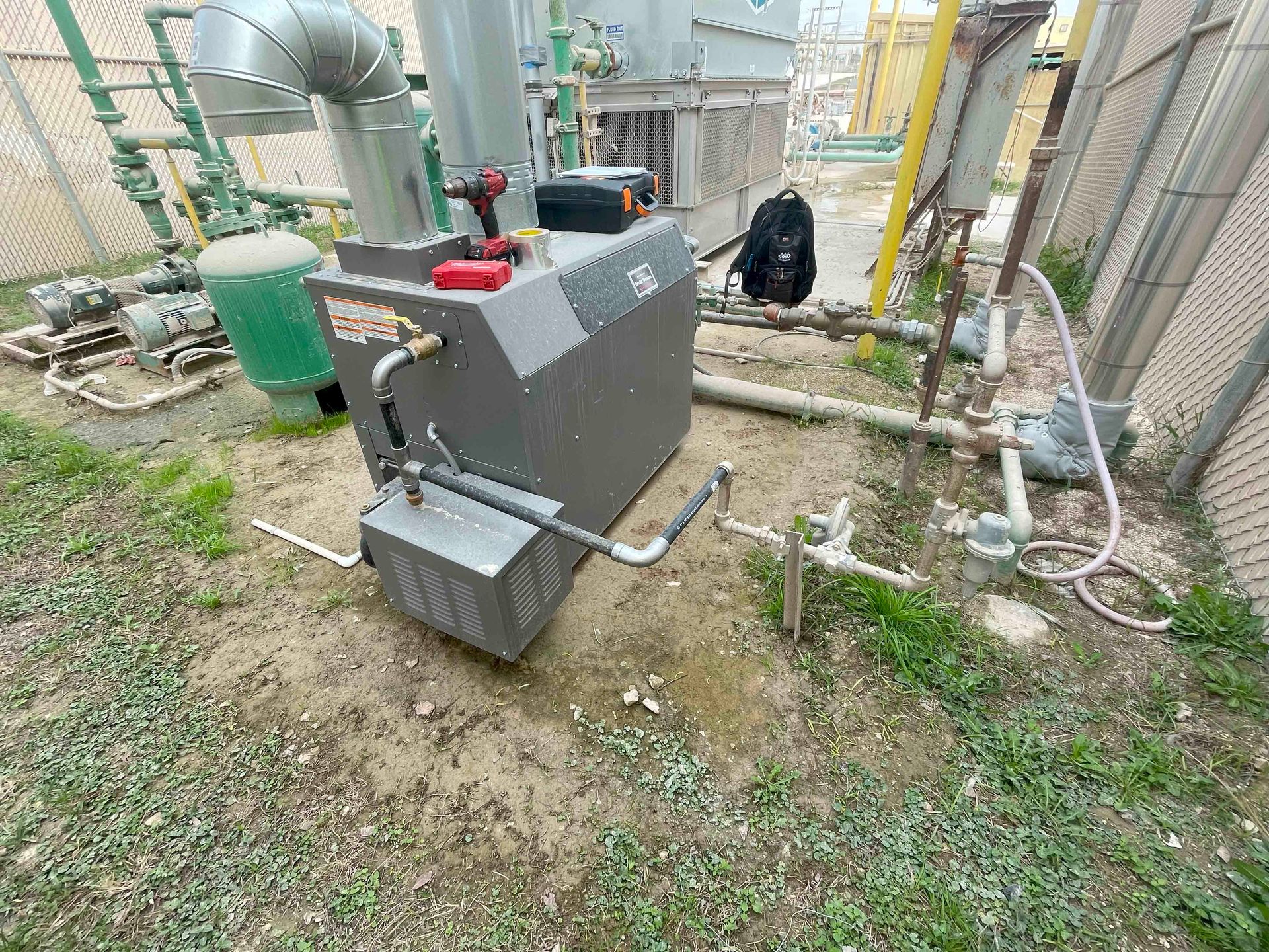 A large machine is sitting on the ground next to a fence.