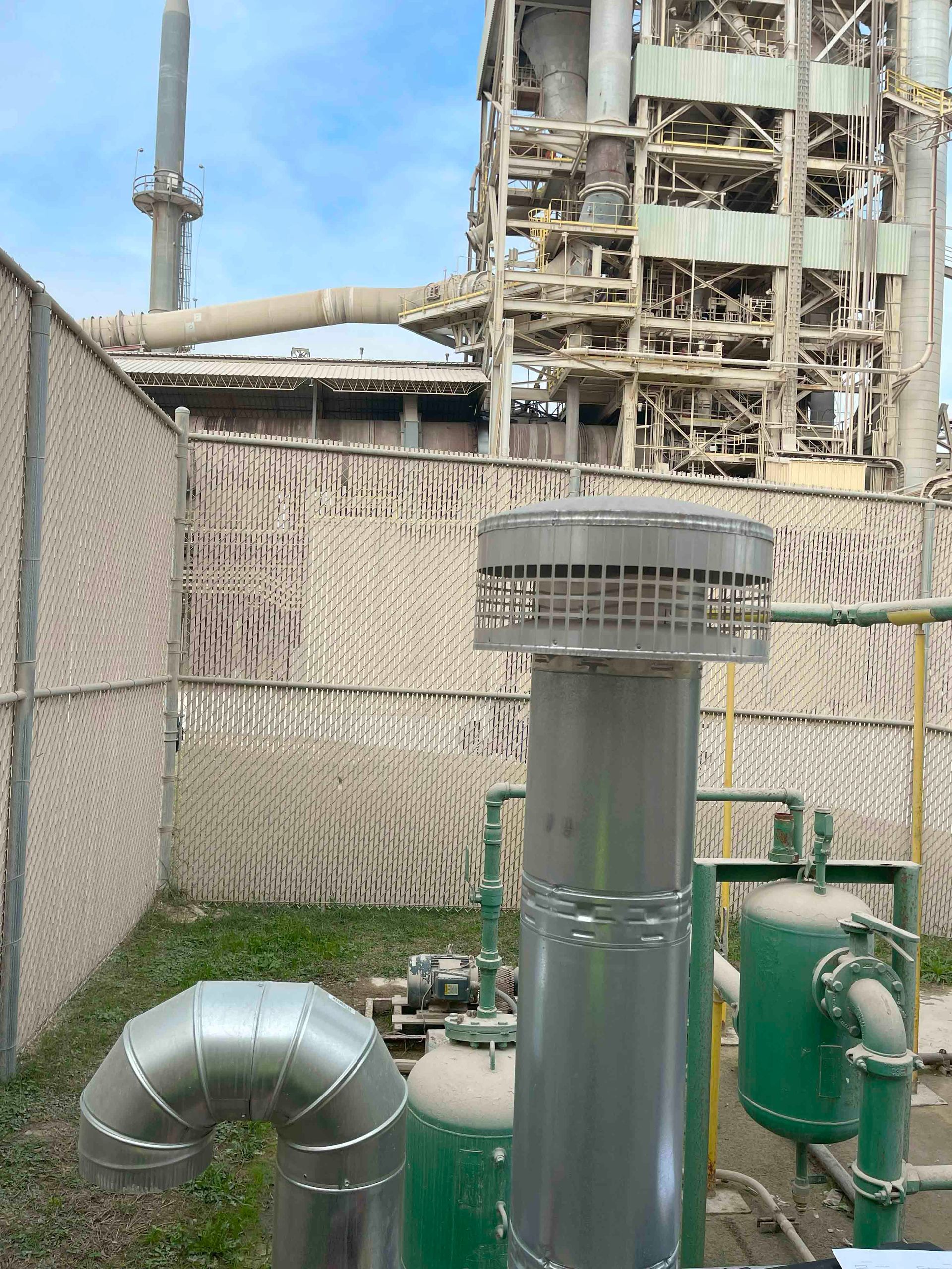 A factory with a fence and pipes in front of it