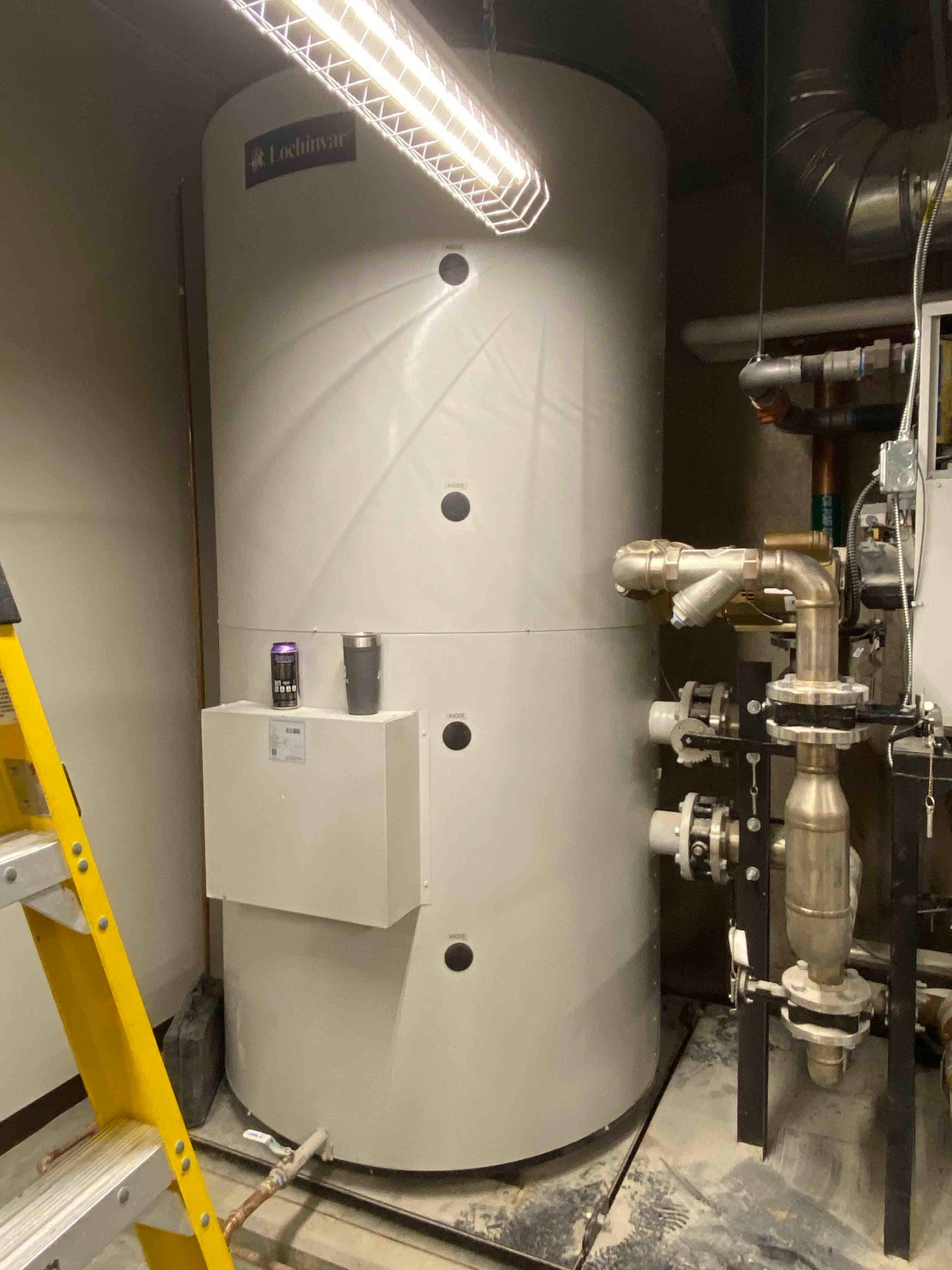 A large white tank is sitting in a room next to a yellow ladder.