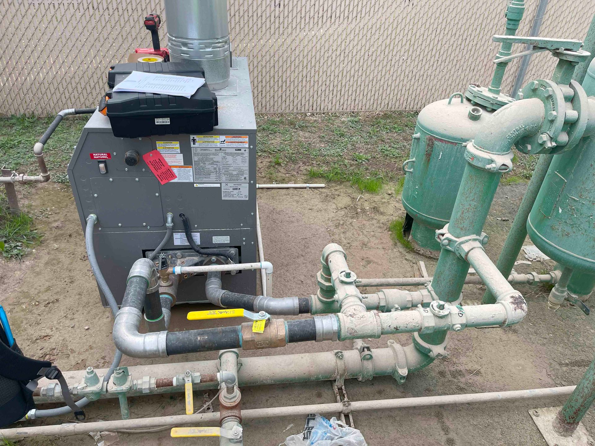 A boiler is sitting on the ground next to a bunch of pipes.