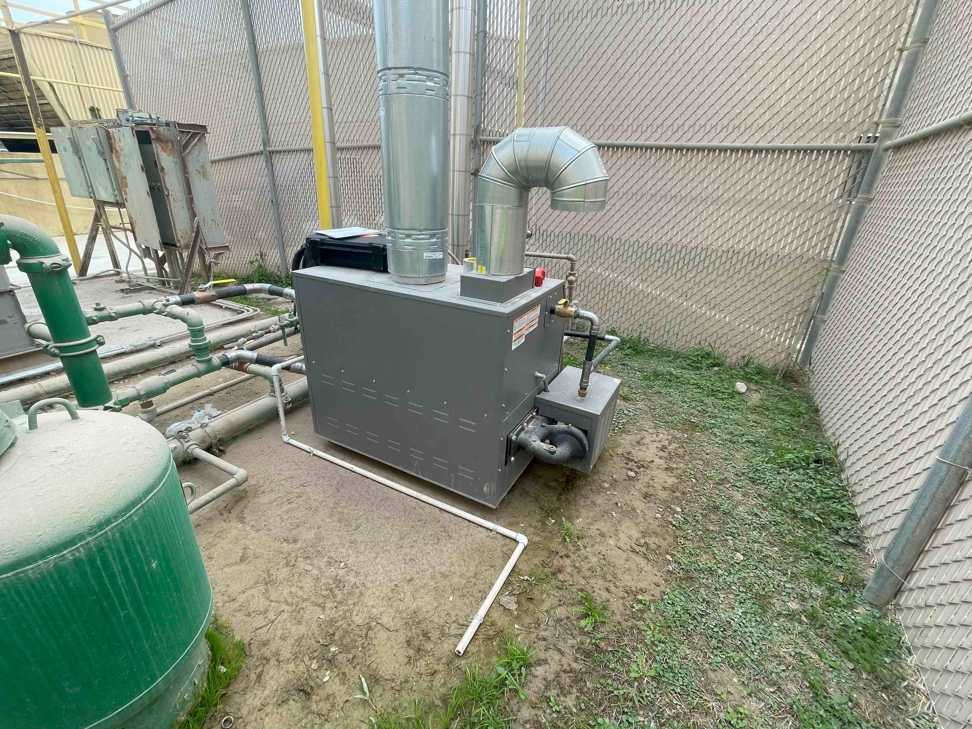 A large machine is sitting in a grassy area next to a chain link fence.