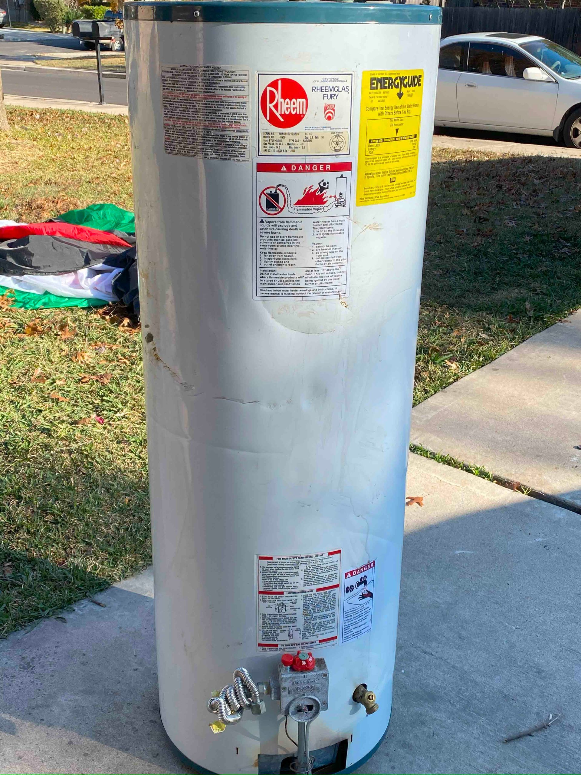 A white water heater is sitting on a sidewalk next to a car.