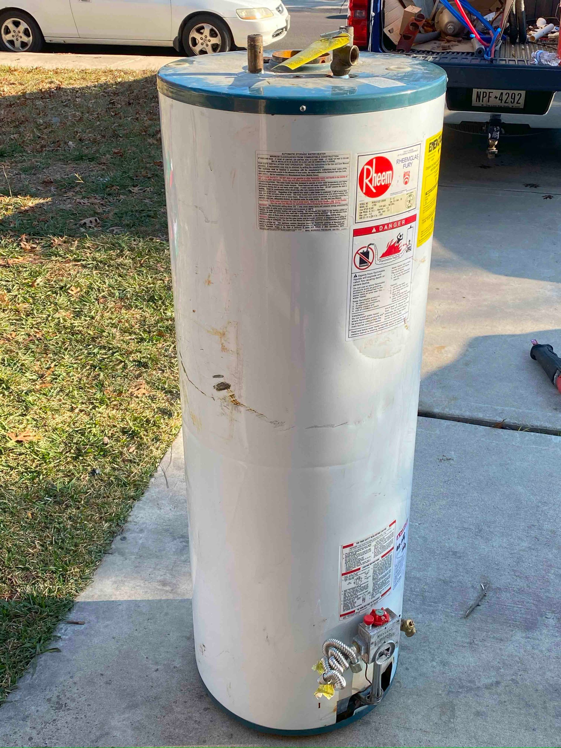 A white water heater is sitting on a sidewalk next to a car.