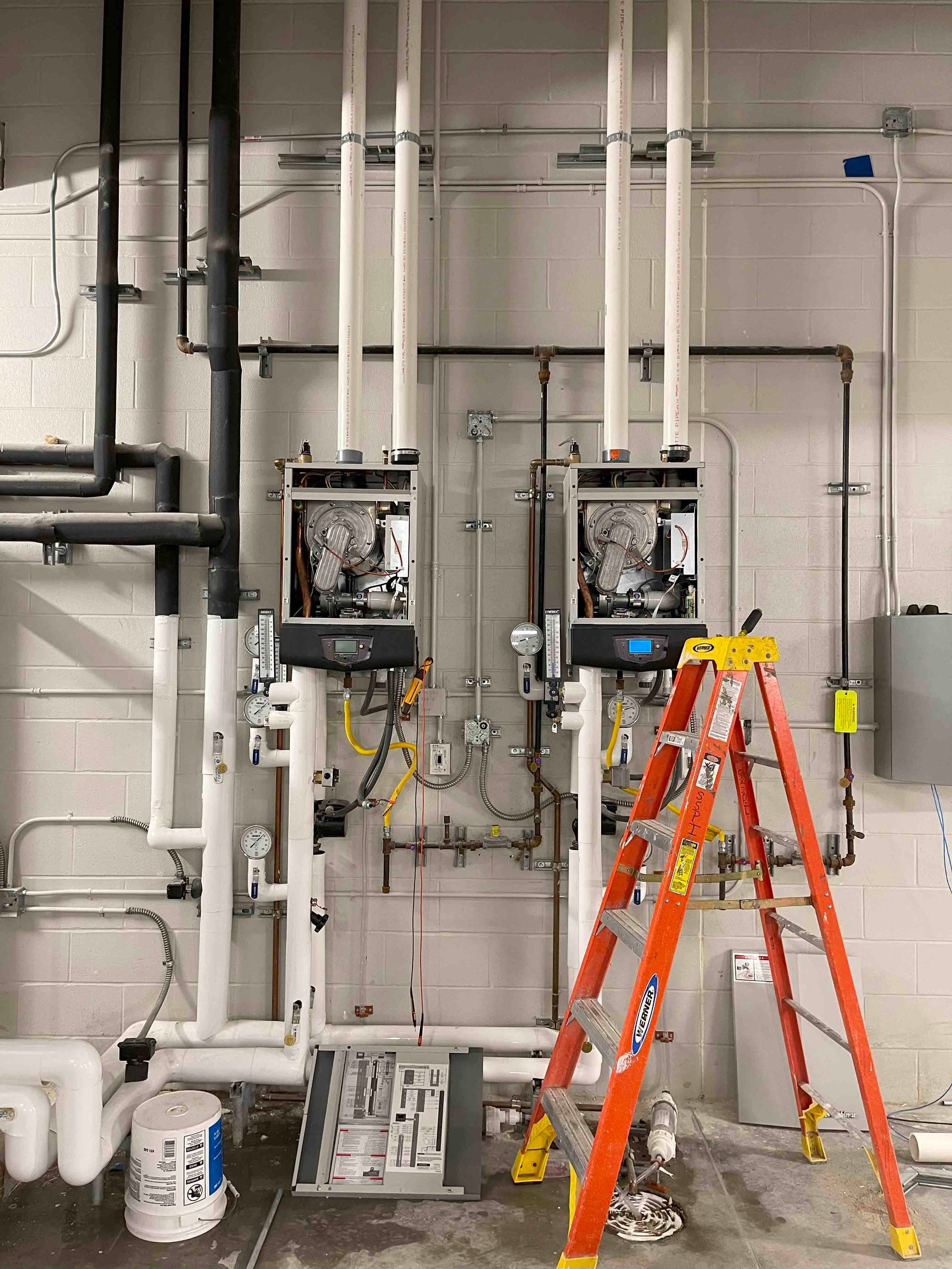 A room with a lot of pipes and a ladder in it.