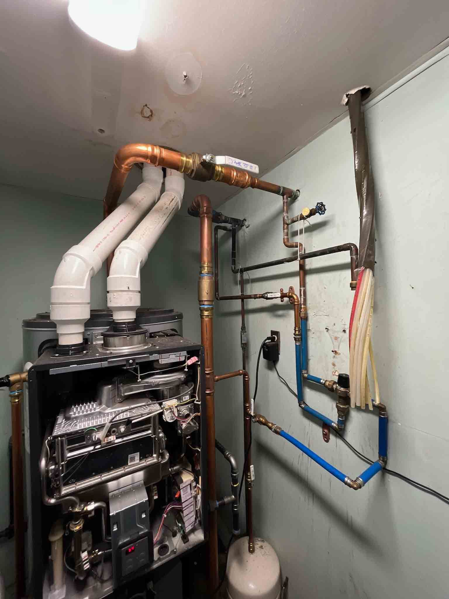 A room with a lot of pipes and a water heater.
