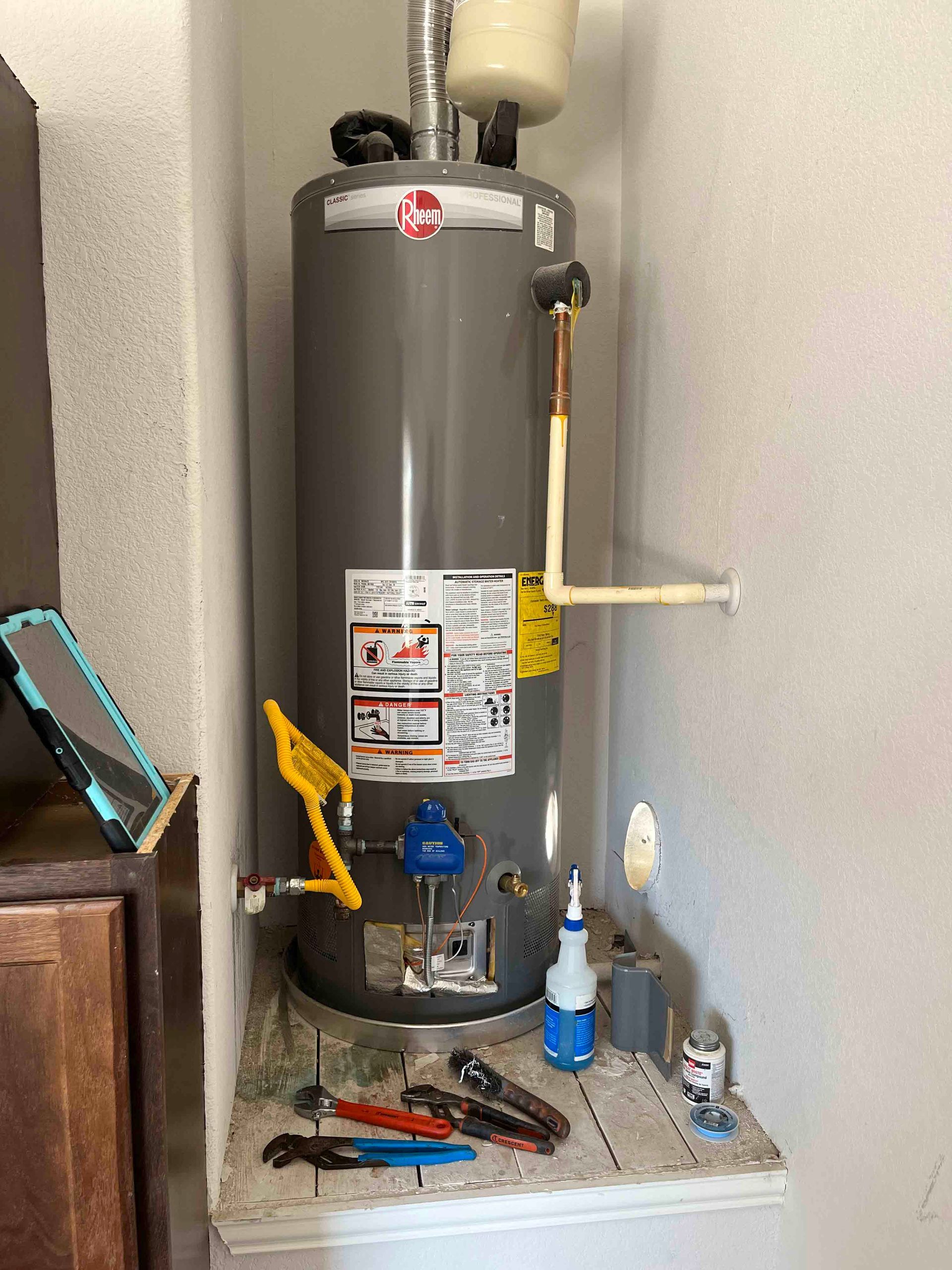 A water heater is sitting in a corner of a room next to a wall.