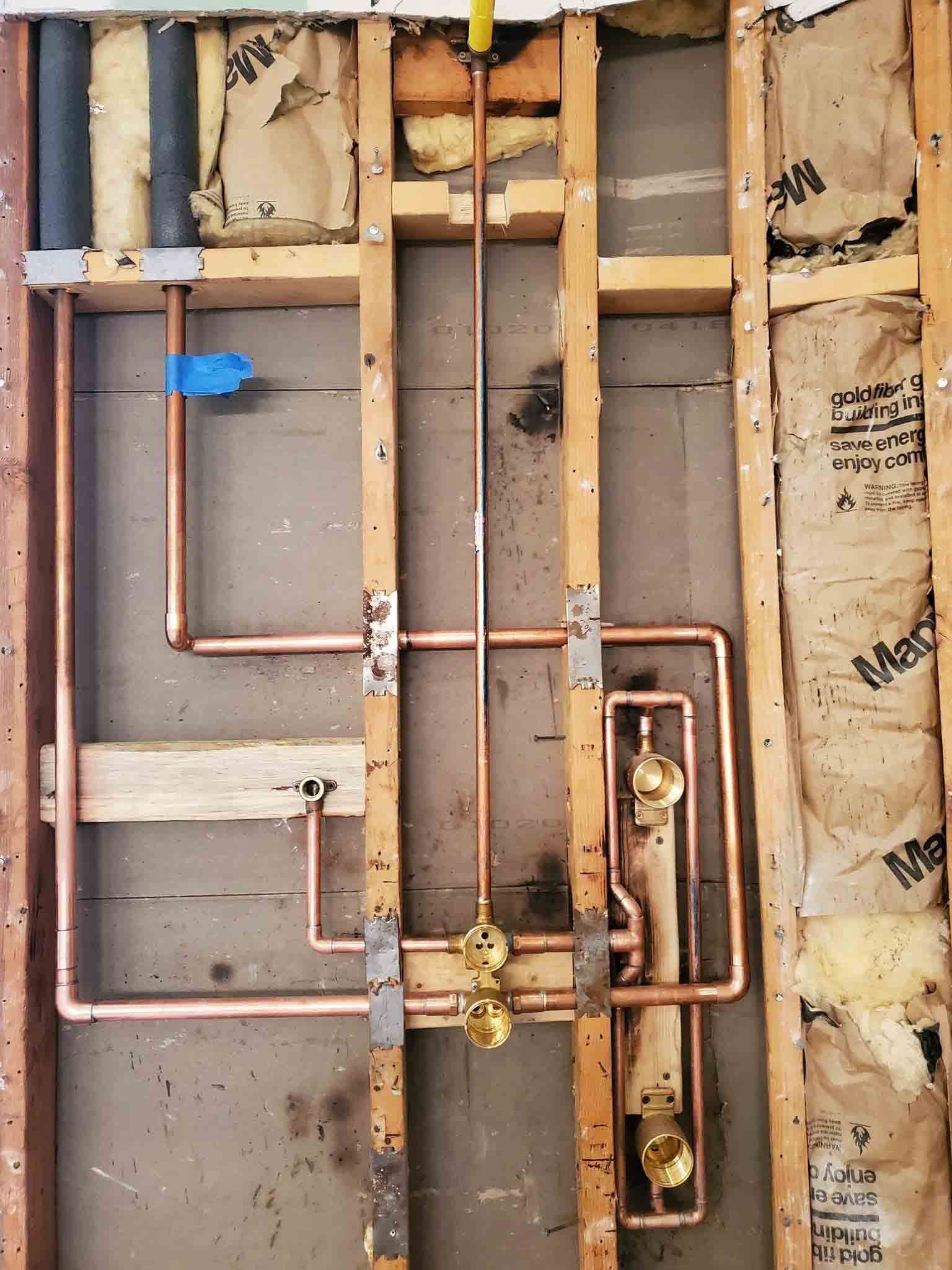 Copper pipes are being installed in a bathroom wall.