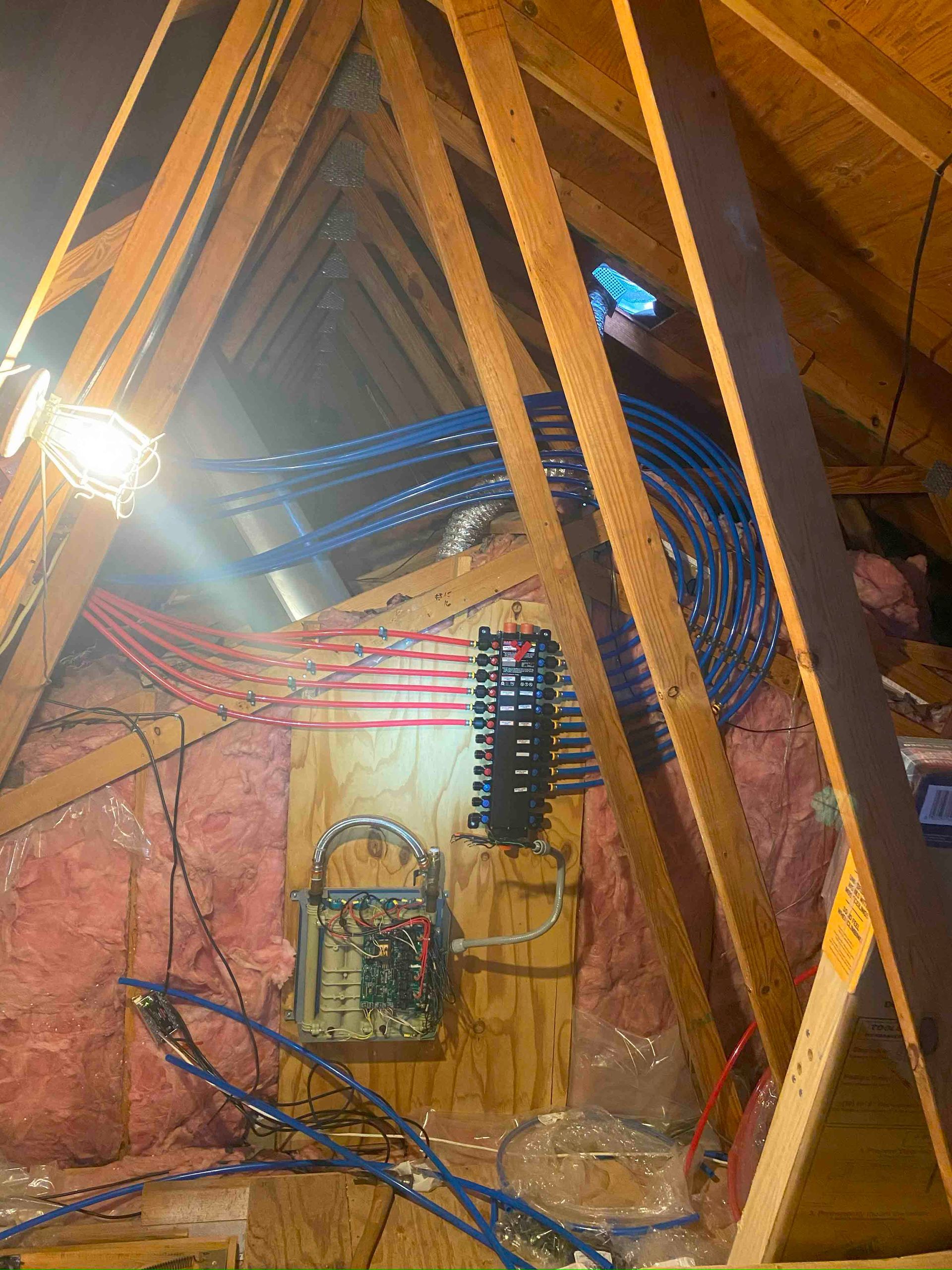 A bunch of wires are hanging from the ceiling of an attic.