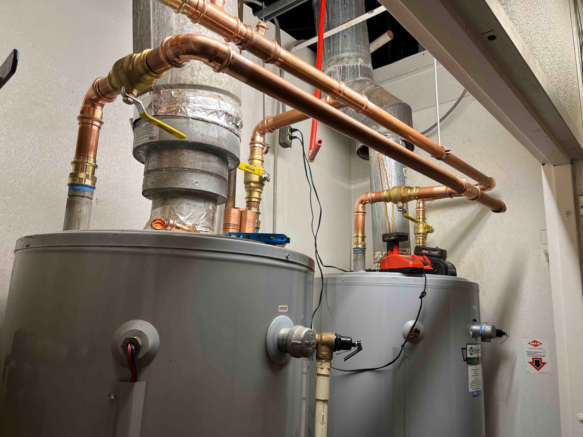 Two water heaters are sitting next to each other in a room with copper pipes.