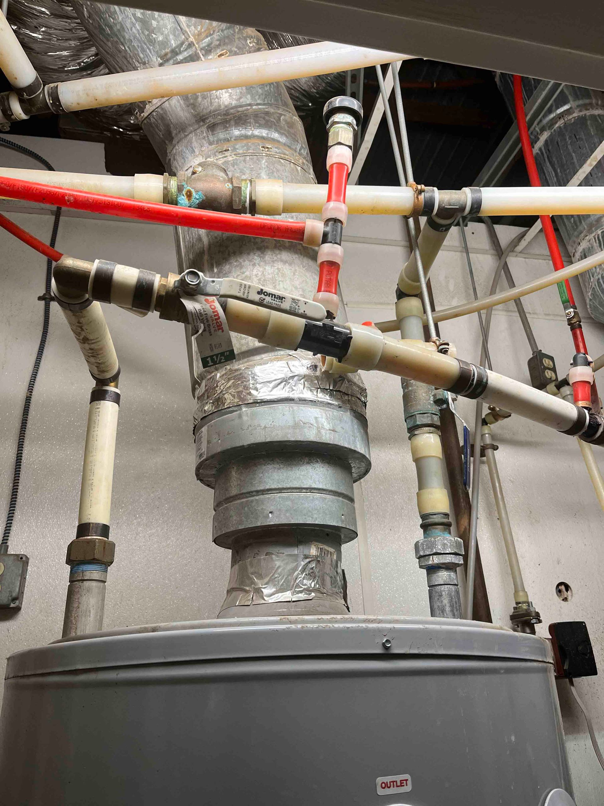A water heater is surrounded by pipes and wires in a room.