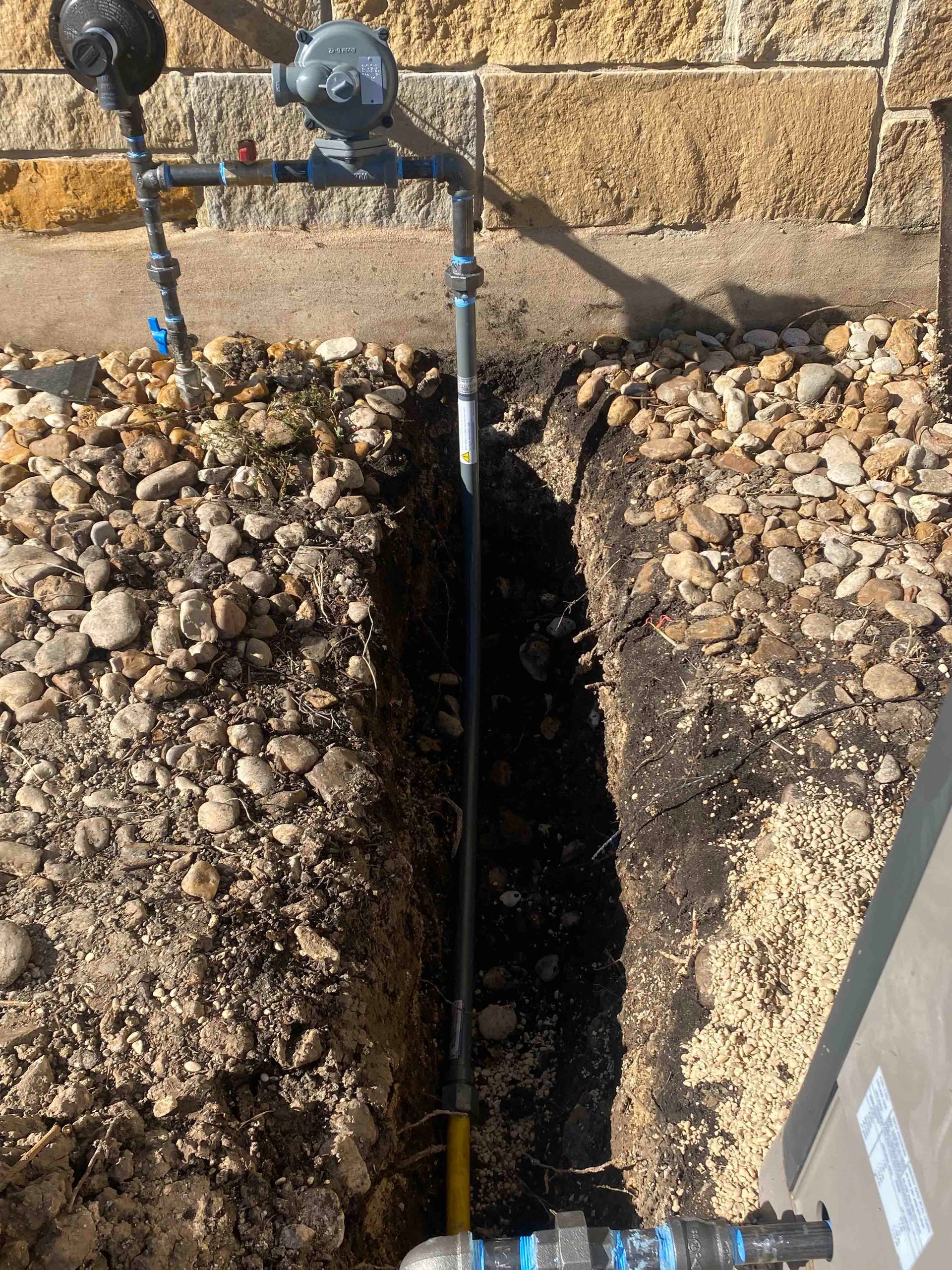 A pipe is being installed in the ground next to a brick wall.