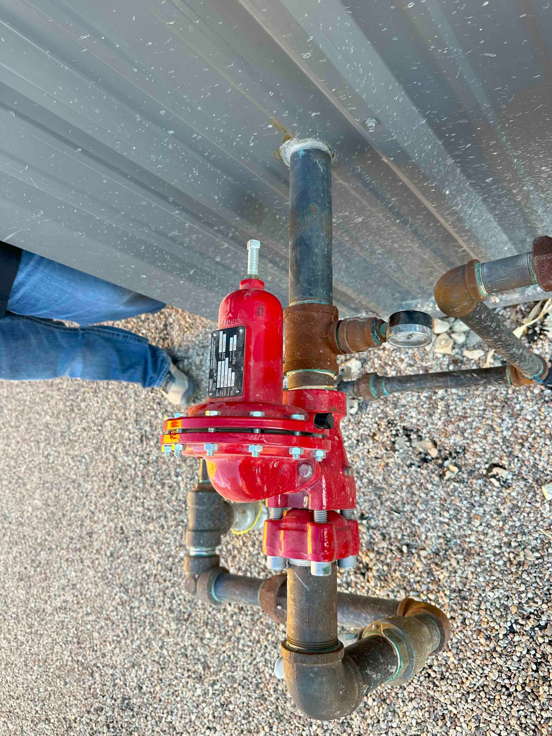 A person is standing next to a red valve on a pipe.