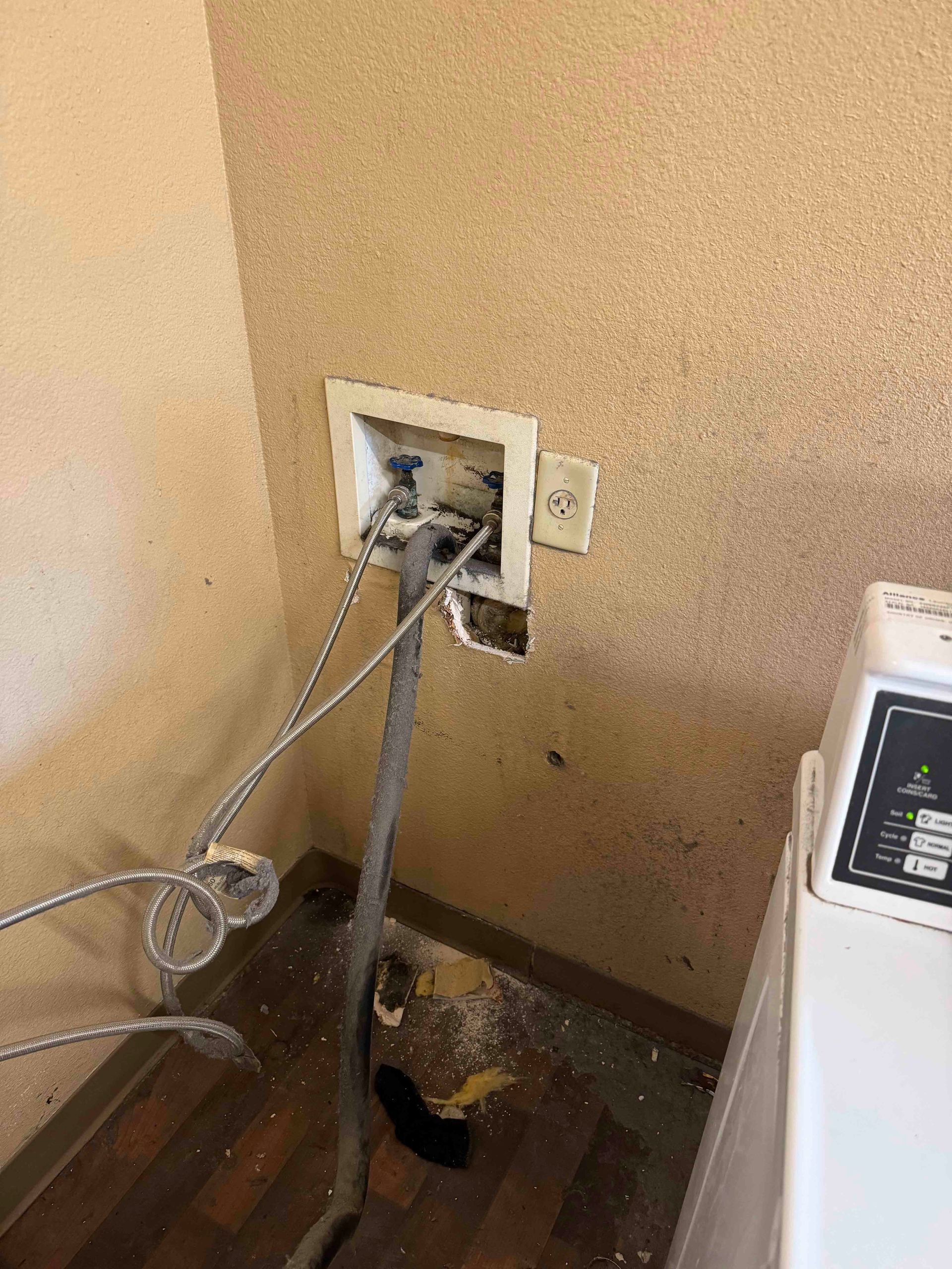 A washer and dryer are in a room with a hole in the wall.