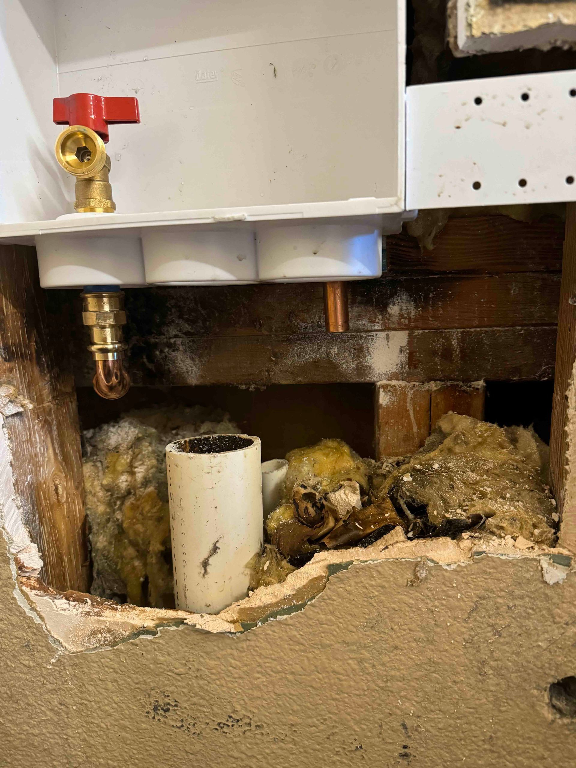 A hole in a wall with a valve and pipes coming out of it.