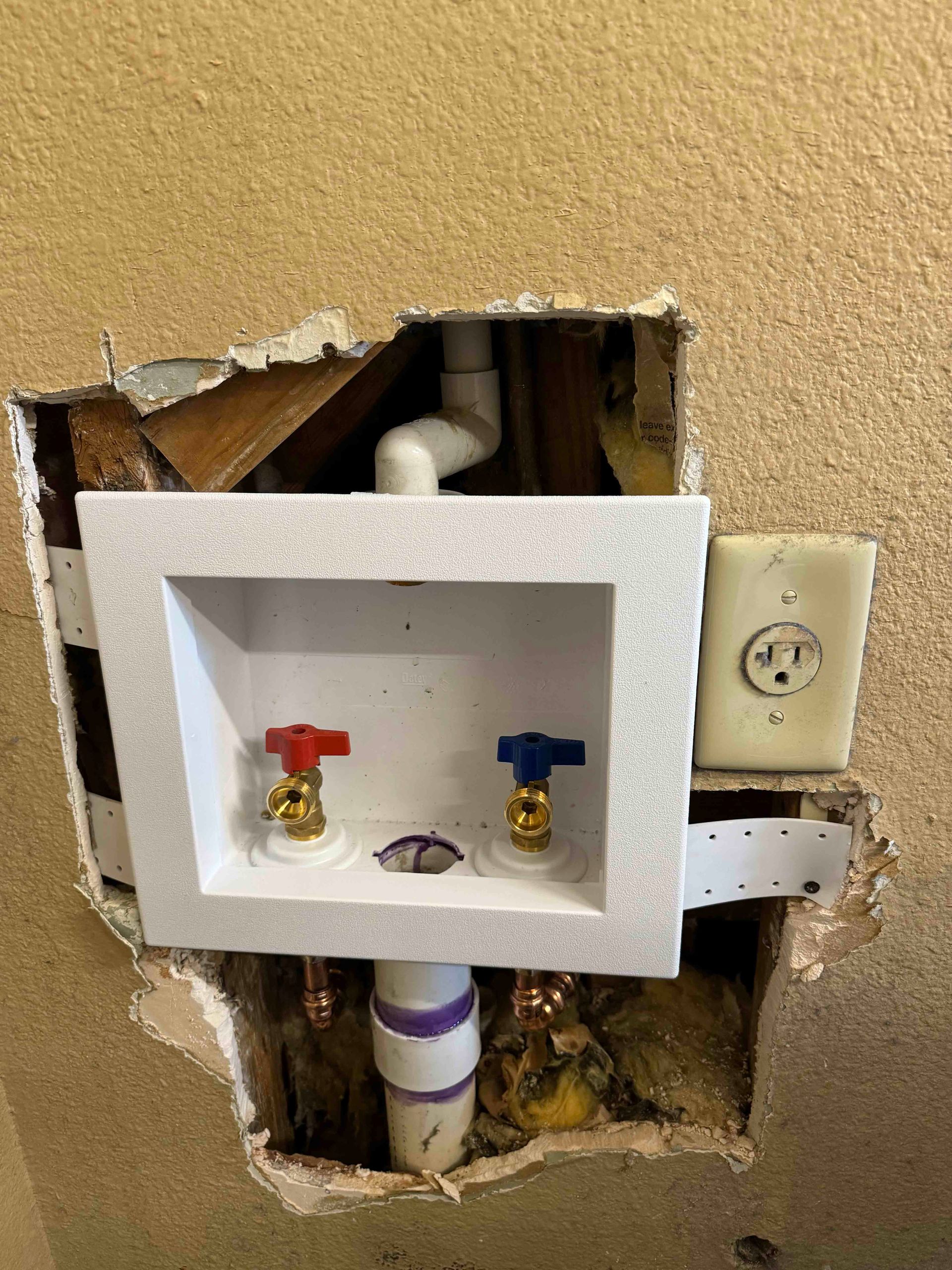 A hole in a wall with a washer and dryer outlet.