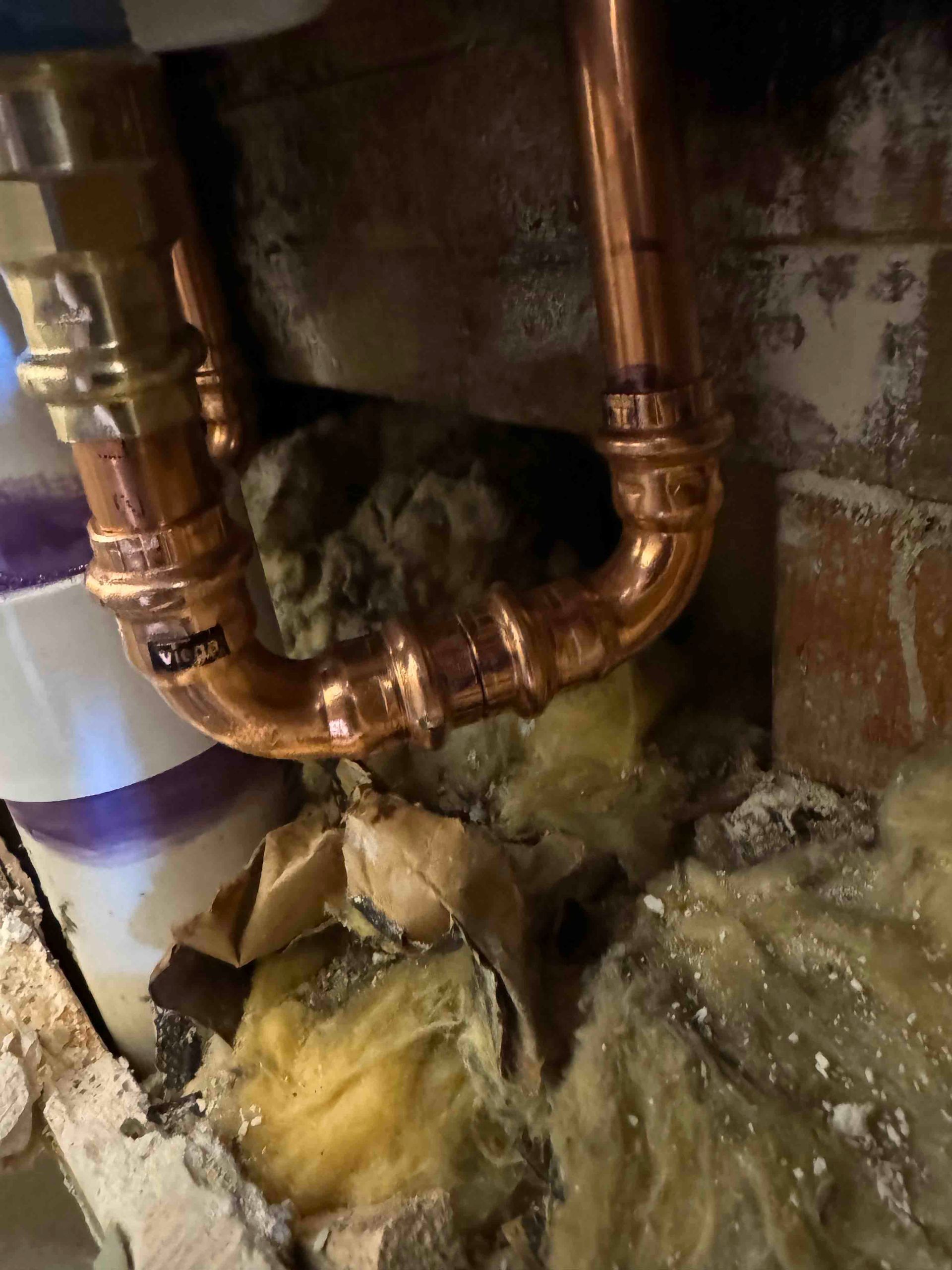 A close up of a copper pipe in a brick wall.