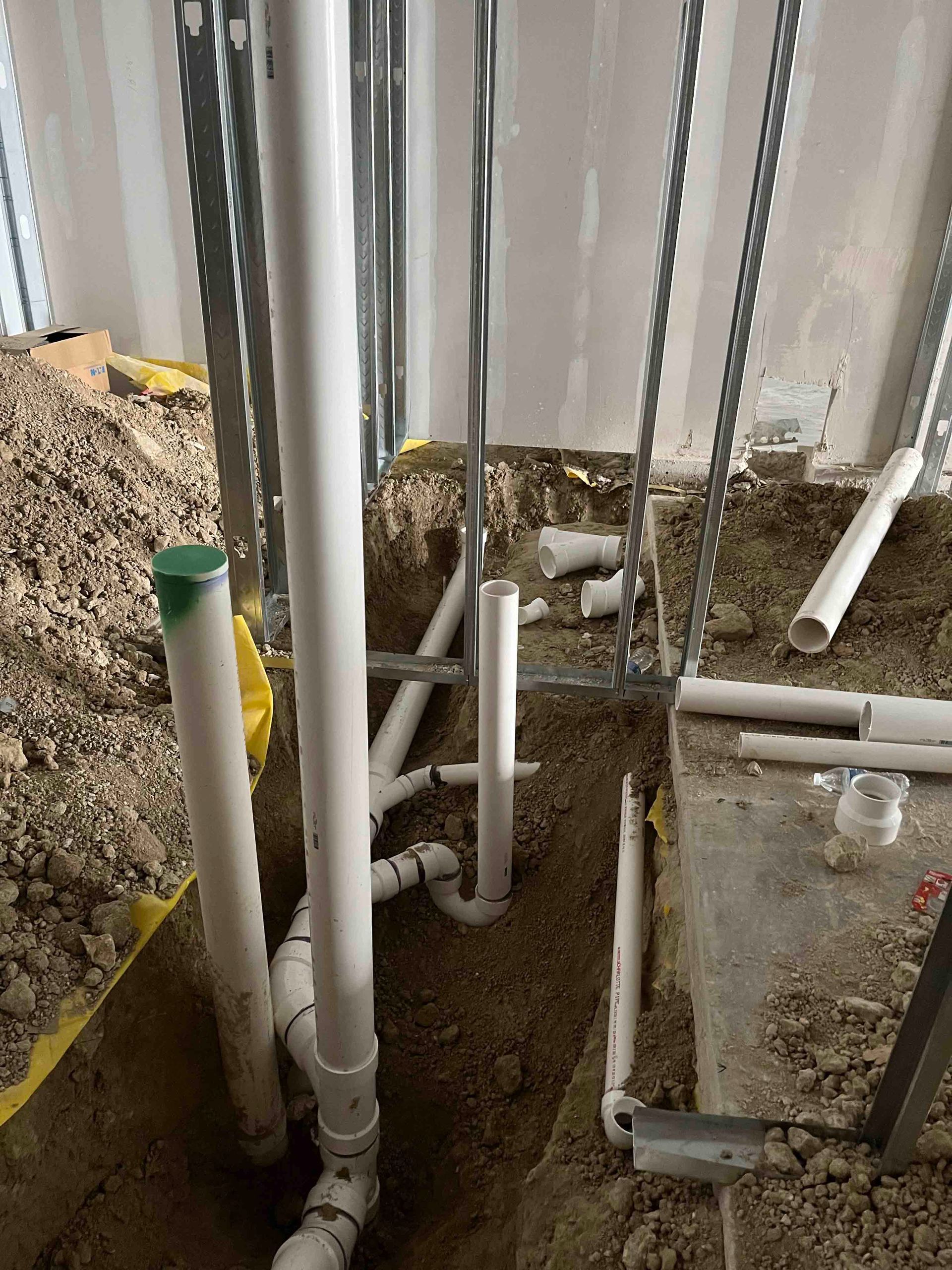 A bunch of pipes are laying in the dirt in a room.