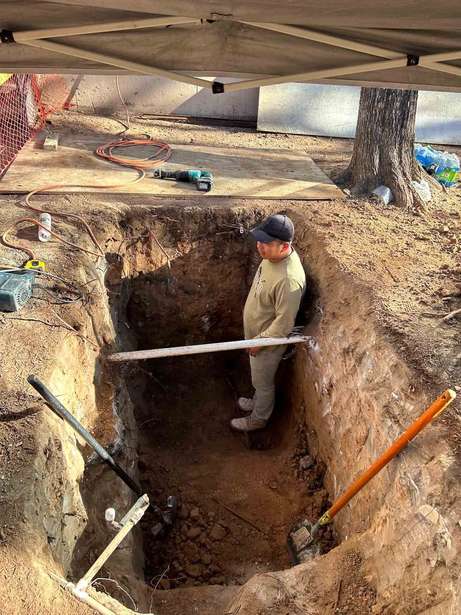 A man is standing in a hole in the ground holding a level.