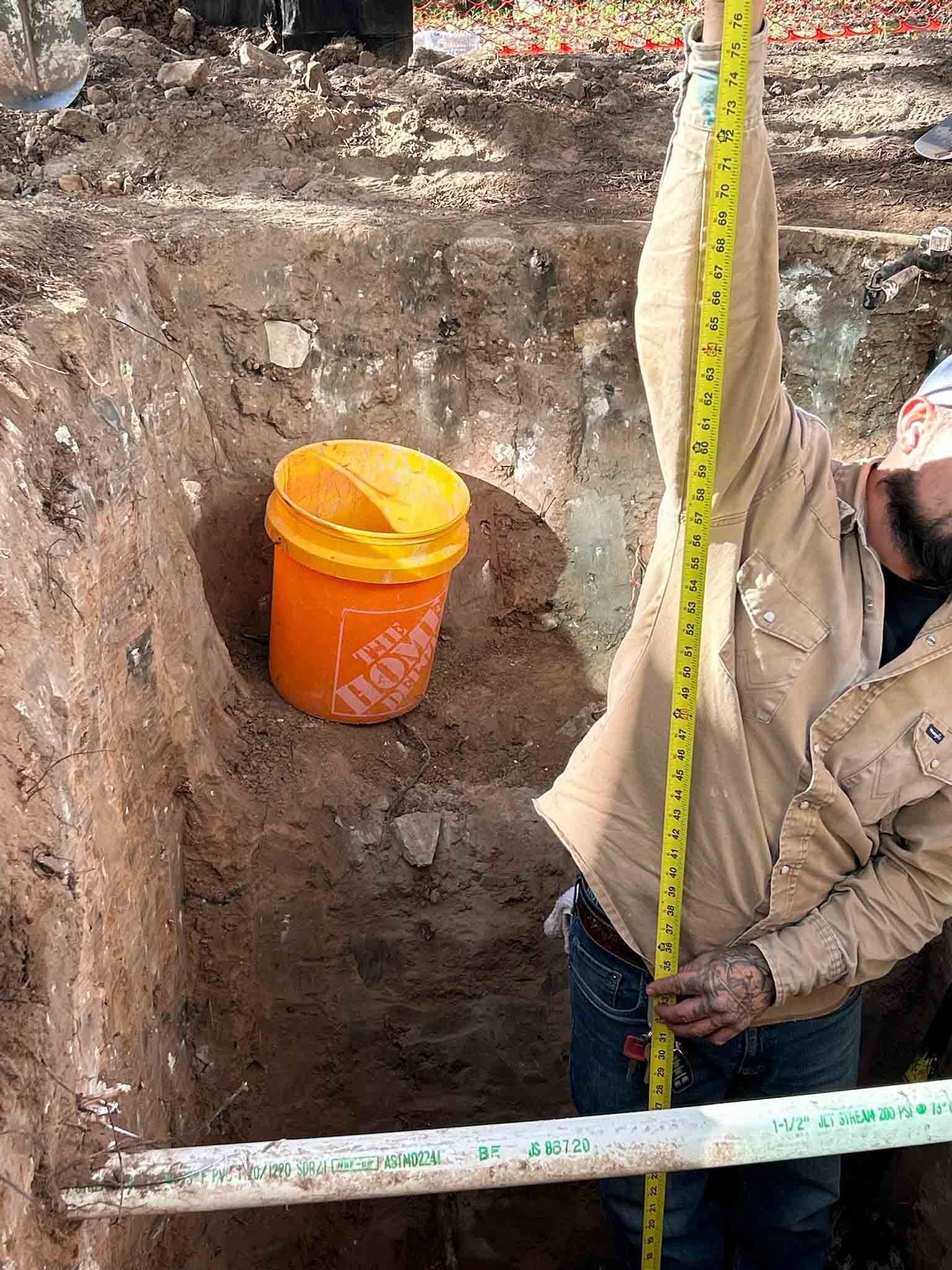 A man is measuring a hole in the ground with a tape measure.