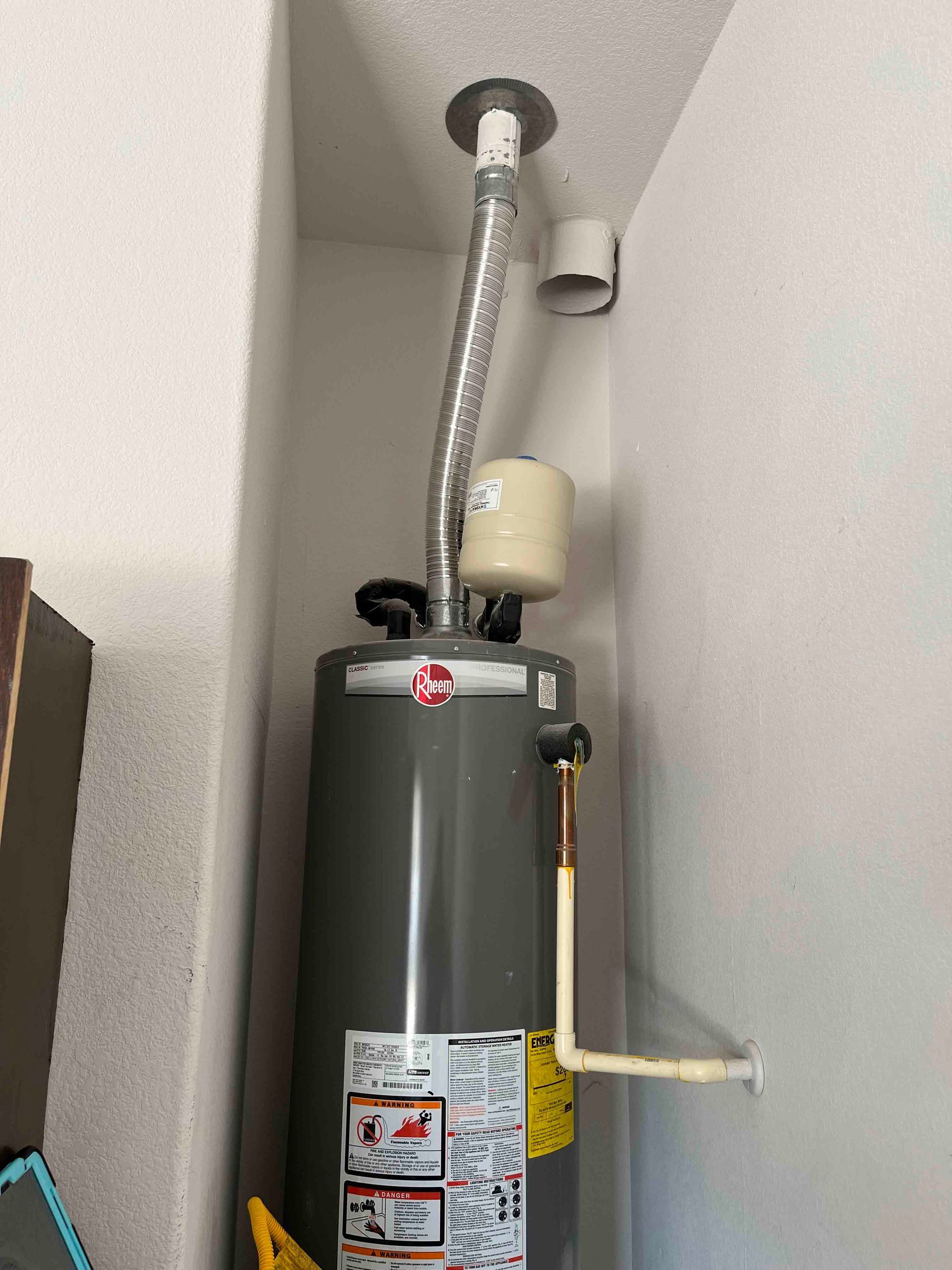 A gray water heater is sitting in a corner of a room.